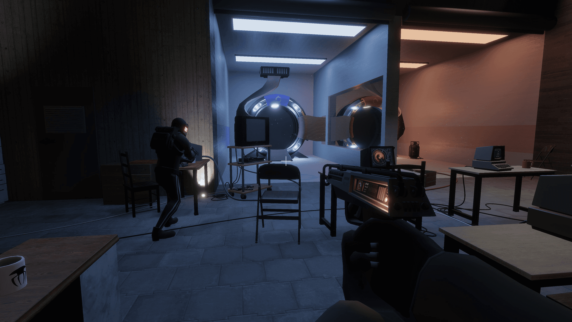First person view inside a building. The player is holding a scifi pistol in a hangar like room that features two big ring shaped devices, multiple desks with old computers, and another player wearing a helmet.